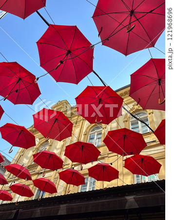 Red umbrellas suspended against a clear blue sky, whimsical and artistic atmosphere. Fusion of creativity and urban architecture, design exterior of outdoor restaurant and hotel. Red umbrellas suspended against a clear blue sky, whimsical and artistic atmosphere. Fusion of creativity and urban architecture, design exterior of outdoor restaurant and hotel. 121968696