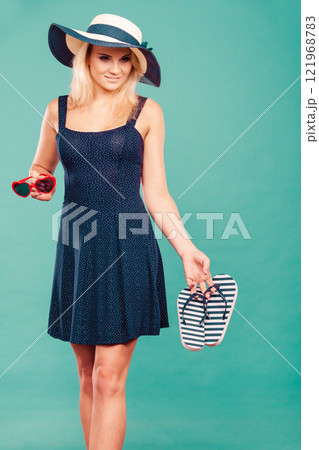 Woman wearing short dress holding flip flops and sunglasses 121968783