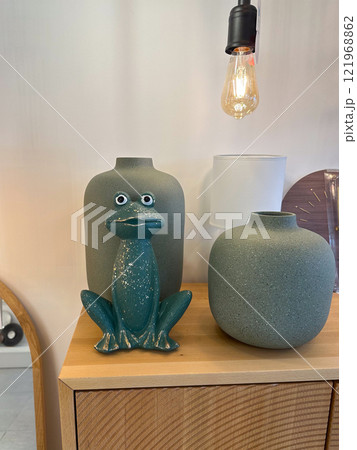 Whimsical ceramic frog and modern minimalist decor create a playful yet elegant ambiance. Combination of textures, colors, and lighting makes this composition both eye-catching and charming. Balancing 121968862