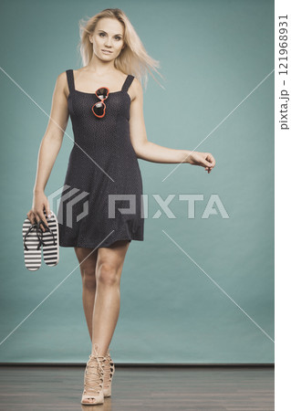 Woman wearing short dress holding flip flops and sunglasses Woman wearing short dress holding flip flops and sunglasses 121968931