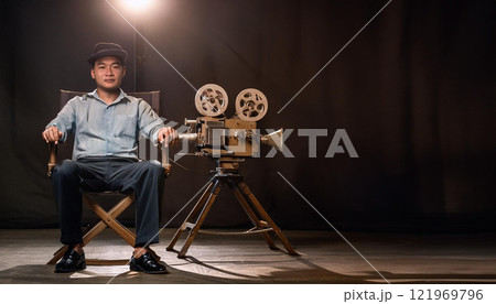 A man sits in a chair in front of a movie camera A man sits in a chair in front of a movie camera 121969796