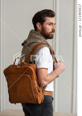 A Stylish and Man standing with a yellow brown backpack in a Contemporary Modern Setting A Stylish and Man standing with a yellow brown backpack in a Contemporary Modern Setting 121969817