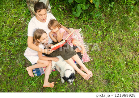 Top shot of a woman reading to her young daughters in a summer garden Top shot of a woman reading to her young daughters in a summer garden 121969929