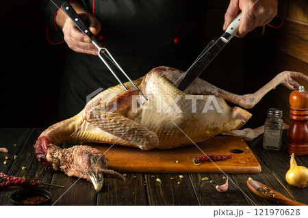 A raw turkey being prepared by the skilled hands of a chef in a dark, cozy kitchen. Spices are scattered on the table to be added to the bird before grilling 121970628