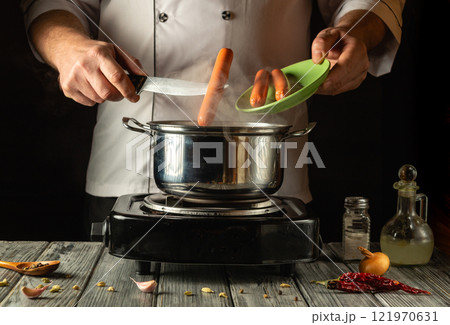 A skilled chef expertly tosses sausages into a bubbling pot on a stovetop, surrounded by colorful ingredients and spices at a cozy kitchen workspace, evoking warmth and culinary creativity A skilled chef expertly tosses sausages into a bubbling pot on a stovetop, surrounded by colorful ingredients and spices at a cozy kitchen workspace, evoking warmth and culinary creativity 121970631