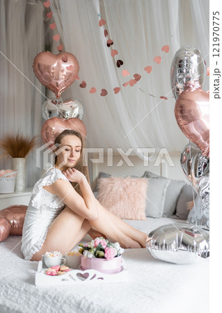 Beautiful young girl at home on the bed in the morning enjoy valentines day celebration with heart shaped balloons Beautiful young girl at home on the bed in the morning enjoy valentines day celebration with heart shaped balloons 121970775