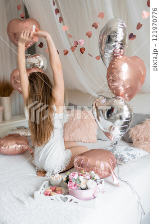 Beautiful young girl at home on the bed in the morning enjoy valentines day celebration with heart shaped balloons Beautiful young girl at home on the bed in the morning enjoy valentines day celebration with heart shaped balloons 121970776