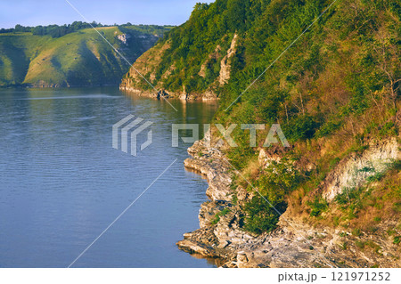 Calm river.Rocky warm hills overgrown with trees and greenery 121971252