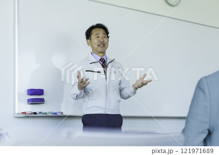 ホワイトボードの前で話をする作業服のミドルエイジの男性　撮影協力：学校法人電波学園 東京電子專門学校 121971689