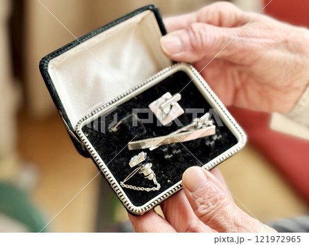 古いカフスボタンとネクタイピンのセットの箱を開けた高齢女性の手元 121972965