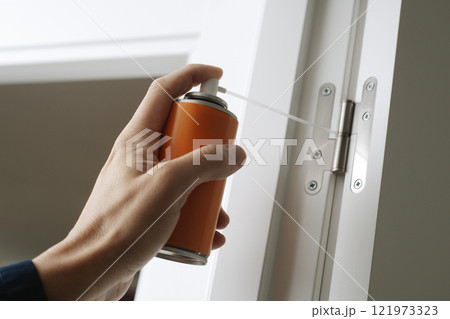 man spraying some lubricating oil on a hinge 121973323