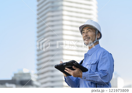 タブレットを持って点検作業をする作業服姿の男性 121973809