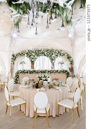Elegant wedding reception hall featuring round tables, white and gold chairs, and floral arrangements Elegant wedding reception hall featuring round tables, white and gold chairs, and floral arrangements 121973975