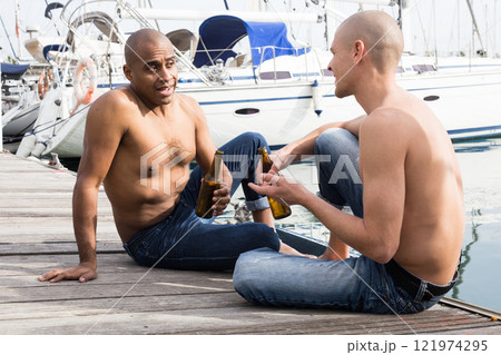 Romantic couple of young men sitting and relaxing together on the pavement in the port Romantic couple of young men sitting and relaxing together on the pavement in the port 121974295