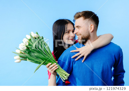 Boy and girl in Valentine day, birthday, or holiday. Young couple with bouquet of white tulips. Portrait of happy brother and sister on blue background. Girl hugging boy Boy and girl in Valentine day, birthday, or holiday. Young couple with bouquet of white tulips. Portrait of happy brother and sister on blue background. Girl hugging boy 121974329