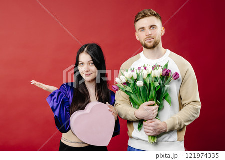 Smiling bearded man giving bouquet of flowers and gift box for beautiful woman. Portrait of happy romantic couple celebration birthday isolated on background 121974335