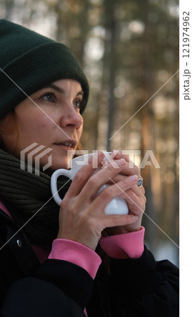 Relaxed young woman in warm winter clothes drinking hot tea outdoors in the backyard of her country house. Nice woman holding a mug with a drink, dreaming, admiring the winter landscape, time for Relaxed young woman in warm winter clothes drinking hot tea outdoors in the backyard of her country house. Nice woman holding a mug with a drink, dreaming, admiring the winter landscape, time for 121974962
