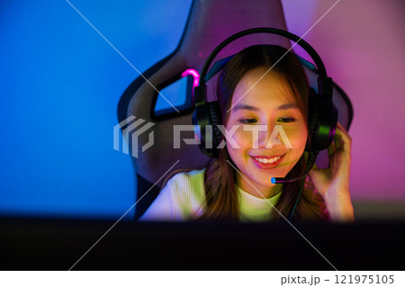Asian happy Gamer endeavor plays online video games tournament with computer neon light, Smile young woman wearing gaming headphones intend to do playing live stream games online at home, font view Asian happy Gamer endeavor plays online video games tournament with computer neon light, Smile young woman wearing gaming headphones intend to do playing live stream games online at home, font view 121975105