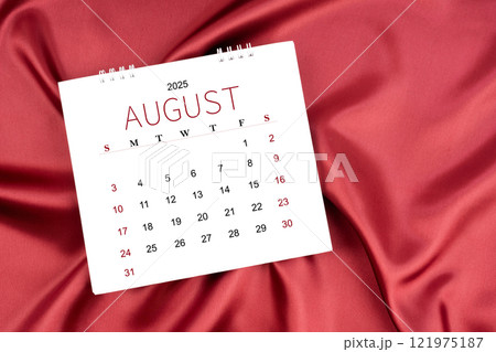 August 2025 Monthly desk calendar on red silk textile background. 121975187