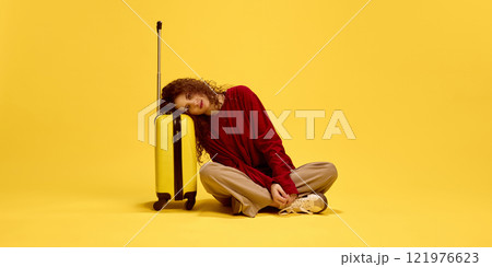 Smiling young lady siting on floor leaning head on suitcase, waiting adventures against yellow studio background. Smiling young lady siting on floor leaning head on suitcase, waiting adventures against yellow studio background. 121976623