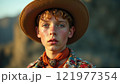 Young cowboy with curly hair and hat against a stunning natural backdrop during golden hour in a western landscape 121977354