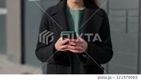 Woman receiving parcel from post terminal machine using smartphone outdoors. 121978069