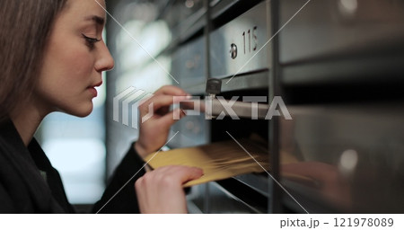 Close up beautiful woman unlocking mailbox and taking mail in apartment building. 121978089