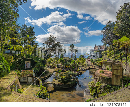A picturesque Monte Palace tropical garden in Funchal on Madeira. Reflective pond surrounded by lush, vibrant greenery and architectural structures 121978151