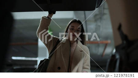 Close-up woman opens the trunk of car and puts paper bags. Shooting from inside the car. Parking in the background. Close-up woman opens the trunk of car and puts paper bags. Shooting from inside the car. Parking in the background. 121978191