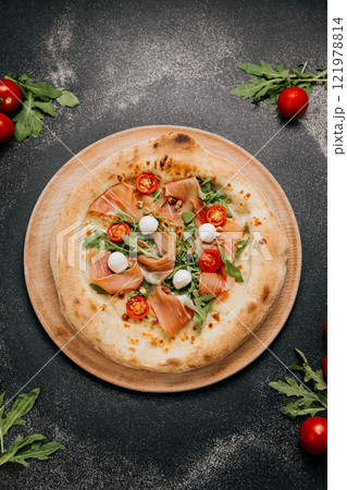 Gourmet pizza topped with fresh prosciutto, arugula, mozzarella, and cherry tomatoes on board 121978814