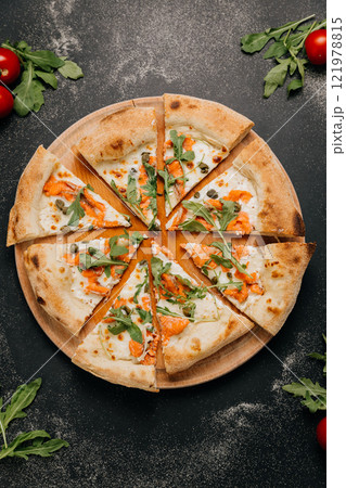 Sliced gourmet pizza with smoked salmon, arugula, and capers on a wooden board for a stylish feast Sliced gourmet pizza with smoked salmon, arugula, and capers on a wooden board for a stylish feast 121978815