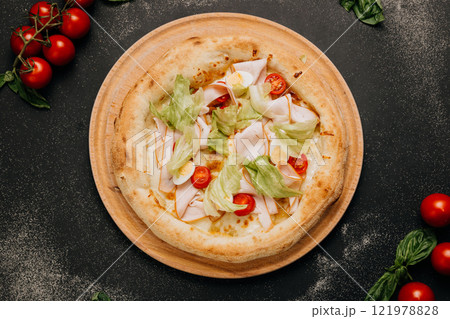 Gourmet salad pizza with lettuce, cherry tomatoes, turkey slices, and cheese on a wooden plate 121978828