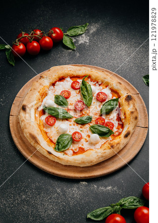 Classic Margherita pizza with cherry tomatoes, mozzarella, and fresh basil on a wooden plate 121978829