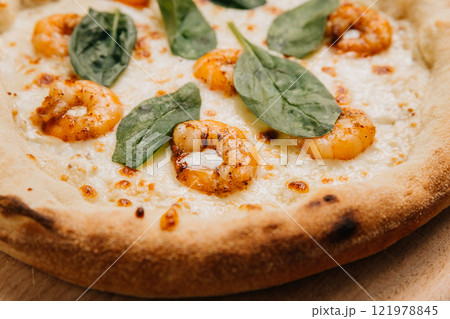 Gourmet shrimp pizza topped with fresh spinach leaves on a golden crust served on a wooden platter 121978845