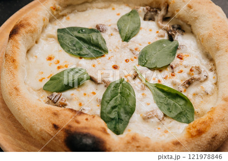 Delicious white pizza with creamy mushrooms, melted cheese, and fresh spinach leaves on wooden plate 121978846