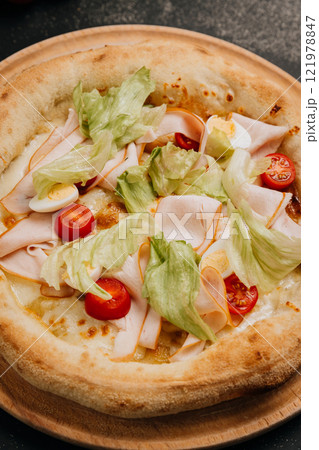 Gourmet salad pizza with lettuce, cherry tomatoes, turkey slices, and cheese on a wooden plate 121978847