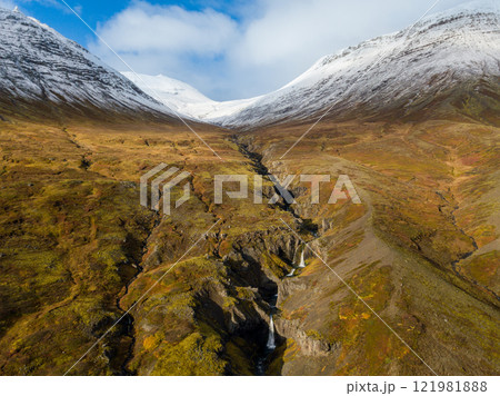 Aerial of Reydarfjordur: Sunlight streaming over a river highlights a vibrant valley leading to majestic snowy mountains in Iceland. Nature's beauty unfolds in a serene landscape filled with color and Aerial of Reydarfjordur: Sunlight streaming over a river highlights a vibrant valley leading to majestic snowy mountains in Iceland. Nature's beauty unfolds in a serene landscape filled with color and 121981888