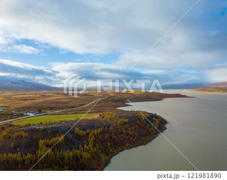Aerial of autumn trees and a lake near Egilsstadir, Iceland, showcasing a sprawling plain with majestic mountains rising in the background Aerial of autumn trees and a lake near Egilsstadir, Iceland, showcasing a sprawling plain with majestic mountains rising in the background 121981890