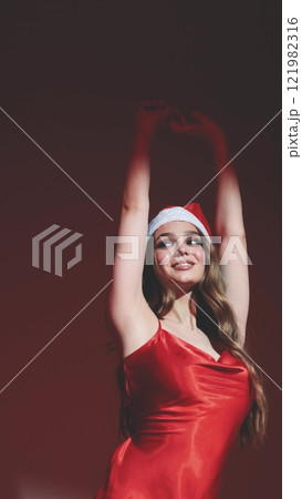 Sexy happy woman with long hair in New Year's hat and red dress posing on white background at New Year's party style photo shoot 121982316