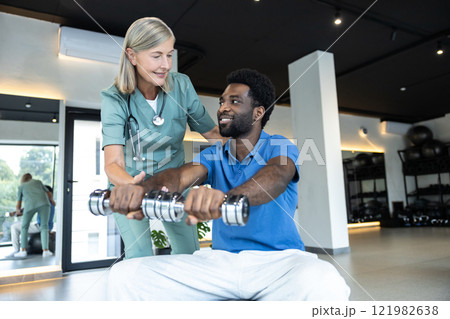 Young male patient exercising with dumbbells with a physical therapist Young male patient exercising with dumbbells with a physical therapist 121982638