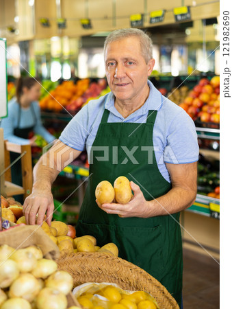 Aged salesman putting potatoes on food stall in greengrocery Aged salesman putting potatoes on food stall in greengrocery 121982690