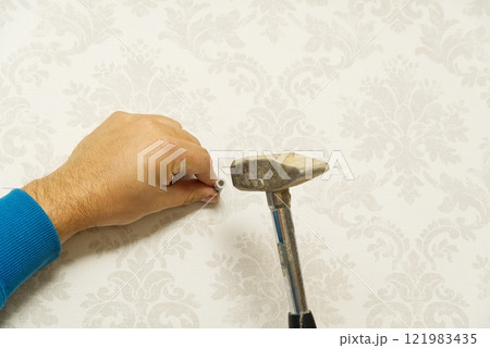 Skilled handyman expertly hammering a nail into a wall while wearing a blue long-sleeve shirt Skilled handyman expertly hammering a nail into a wall while wearing a blue long-sleeve shirt 121983435