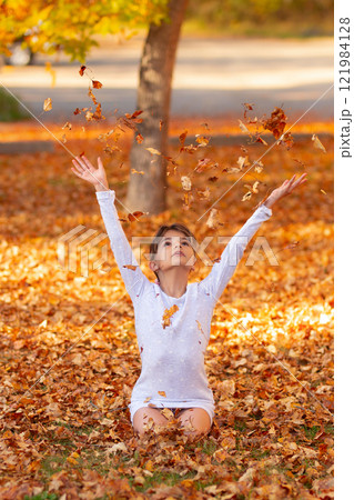 Girl is sitting on the ground in the fall park and throwing yellow leaves. Girl is sitting on the ground in the fall park and throwing yellow leaves. 121984128
