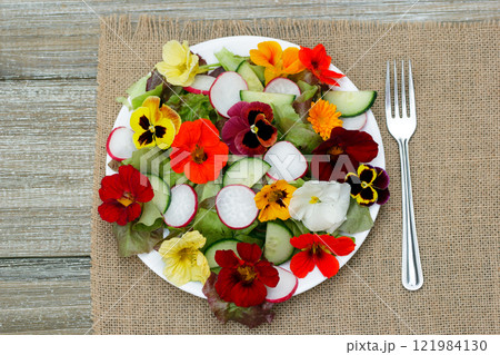 Healthy vegetarian salad of edible nasturtiums, pansies, lettuce and radish on the wooden table with a fork on a plate. Healthy vegetarian salad of edible nasturtiums, pansies, lettuce and radish on the wooden table with a fork on a plate. 121984130