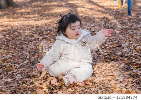【落ち葉で敷き詰められた冬の公園で遊ぶ1歳児　座る】 121984274