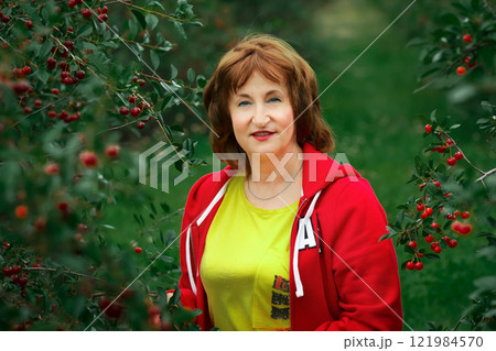 Senior lady is in the sour cherry orchard with ripe berries. 121984570