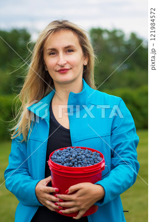 Blond lady with a pale of ripe blueberries in the summer orchard. Blond lady with a pale of ripe blueberries in the summer orchard. 121984572