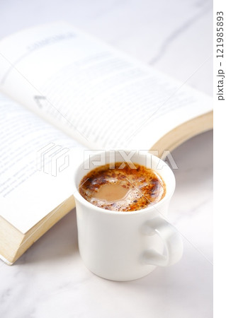 ページを開いたペーパーバック(洋書)とコーヒーの入ったコーヒーカップで、コーヒーを飲みながら読書中 ページを開いたペーパーバック(洋書)とコーヒーの入ったコーヒーカップで、コーヒーを飲みながら読書中 121985893