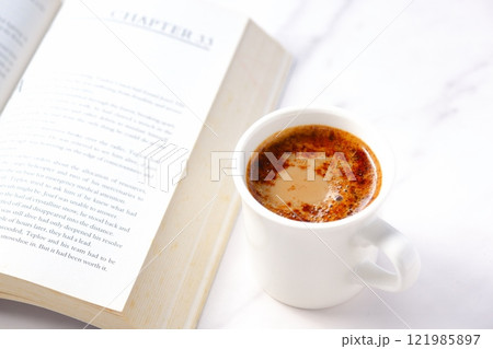 ページを開いたペーパーバック（洋書）とコーヒーの入ったコーヒーカップで、コーヒーを飲みながら読書中 121985897