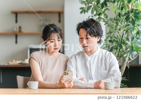 家でスマートフォンを見ながら驚く夫婦・カップル(ニュース・投資・株) 家でスマートフォンを見ながら驚く夫婦・カップル(ニュース・投資・株) 121986622